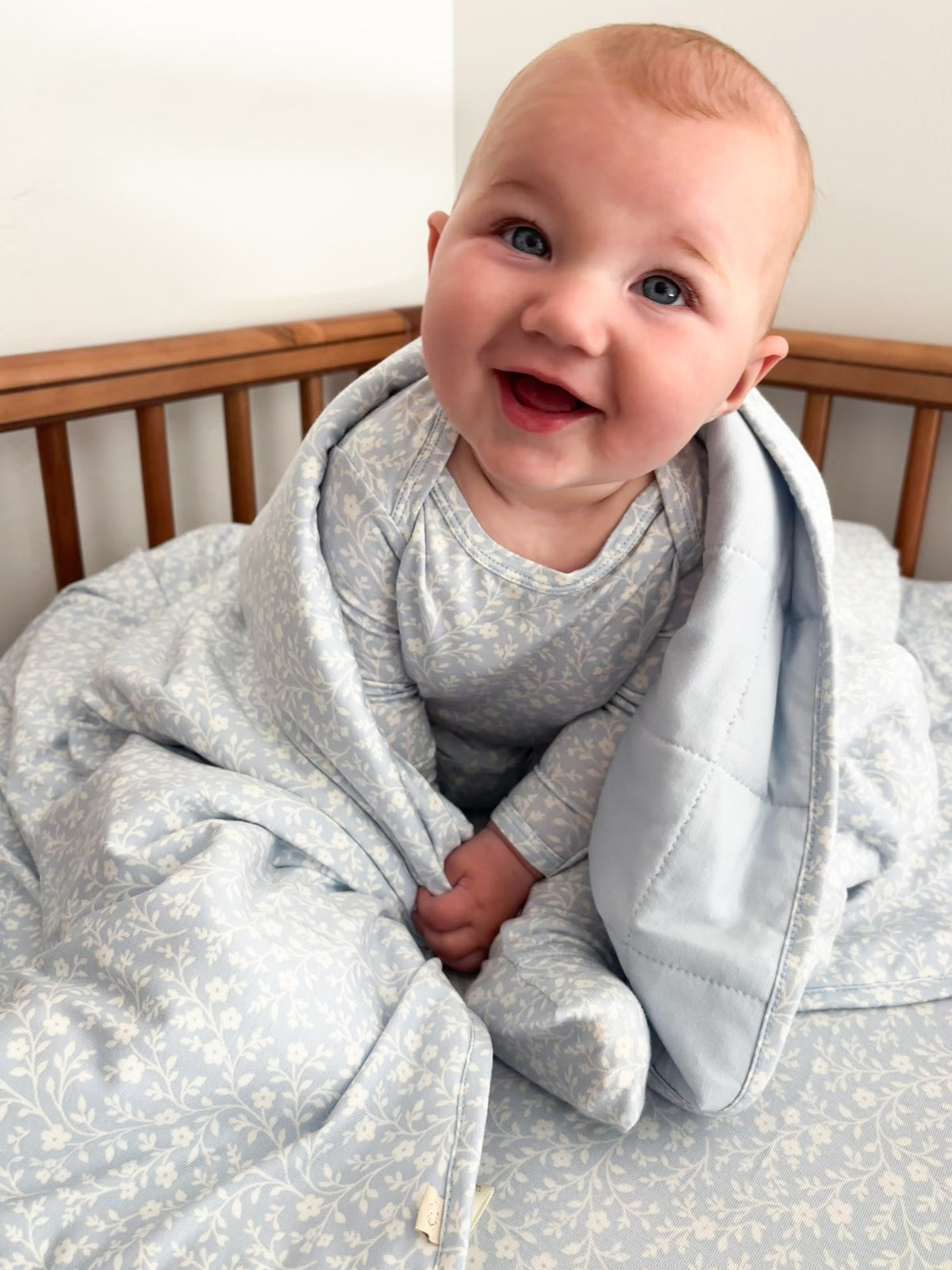 Baby cloud blanket in light blue with white floral pattern and hood, wrapped around infant