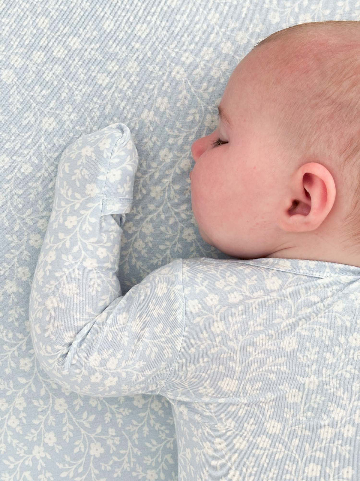 Light blue floral convertible pajama with long sleeves on a lying baby.