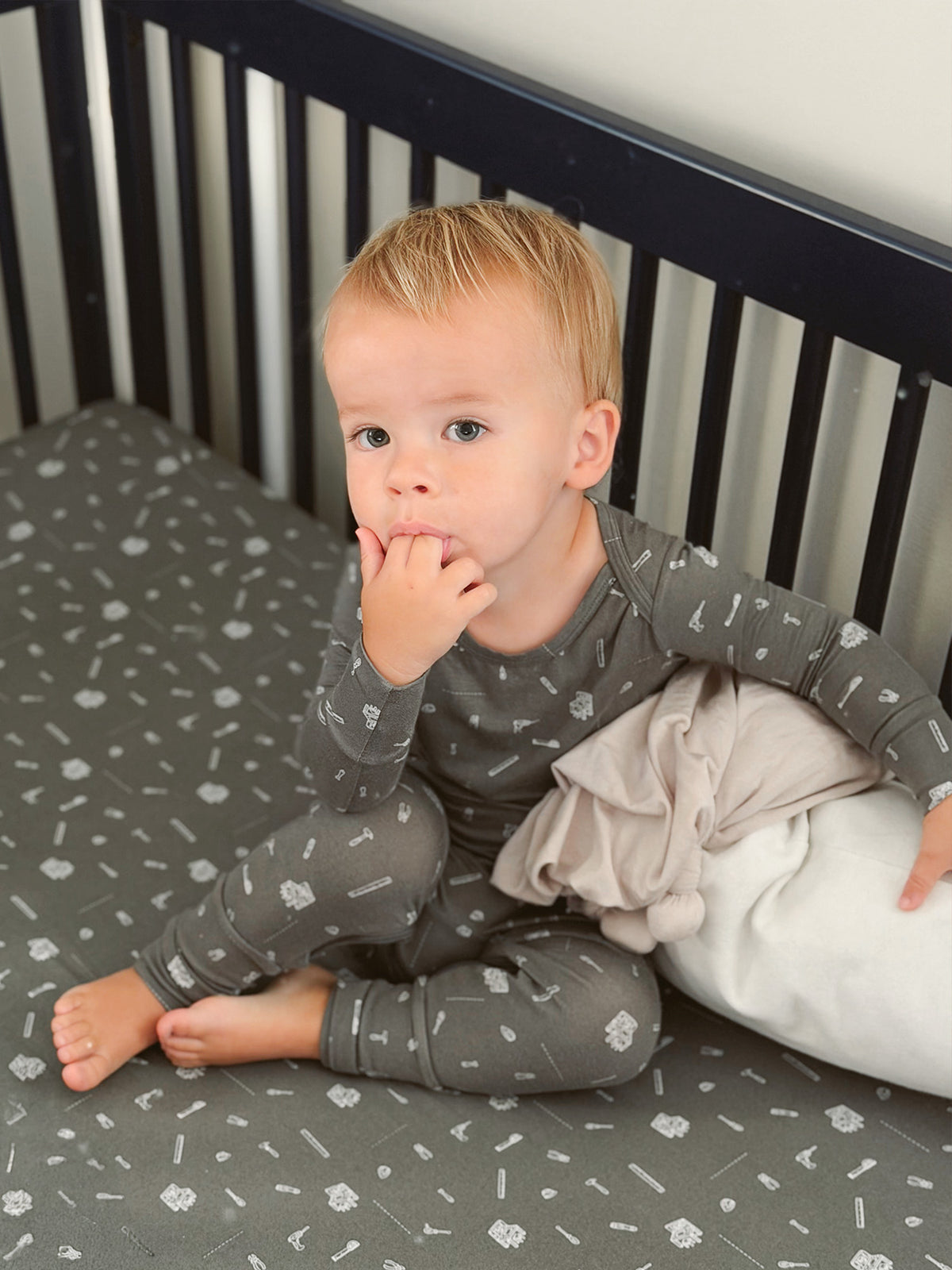 Convertible dark gray pajama with white tool icons, long sleeves and pants, infant lying