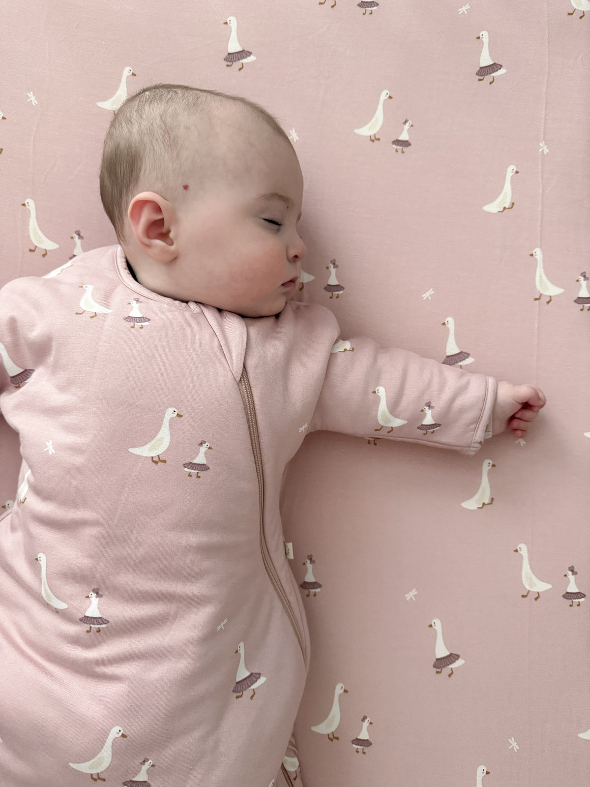 Light pink fitted crib sheet with repeating white goose pattern, smooth cotton