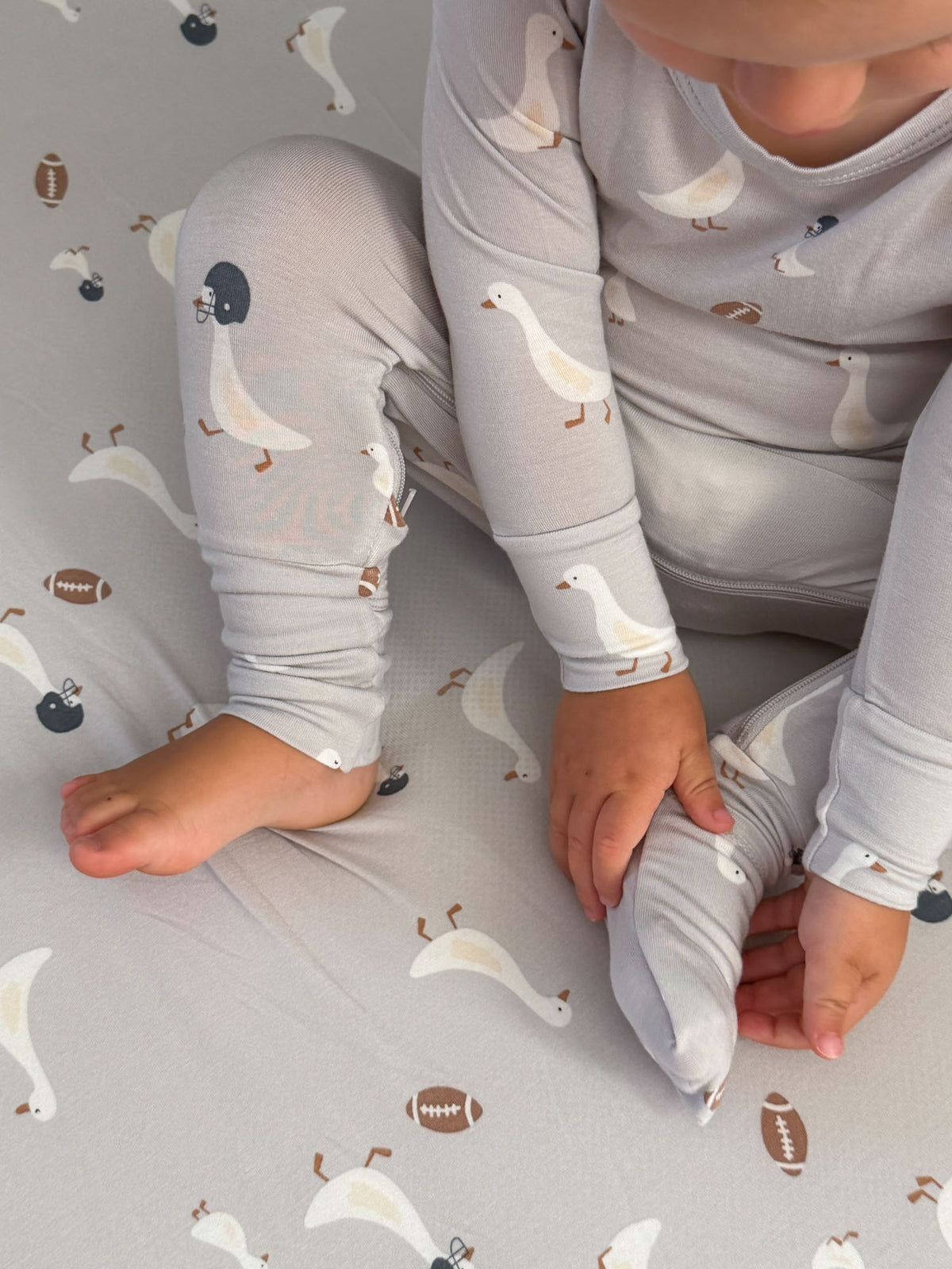 Light gray baby footed pajama with goose and football print and foldover cuffs