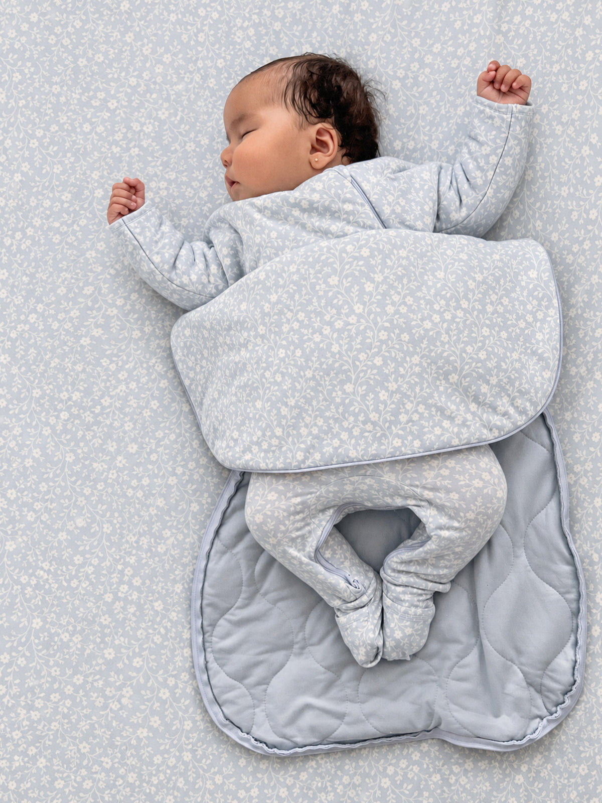 Quilted long-sleeve swaddle sack in light blue with small floral print, open foot flap