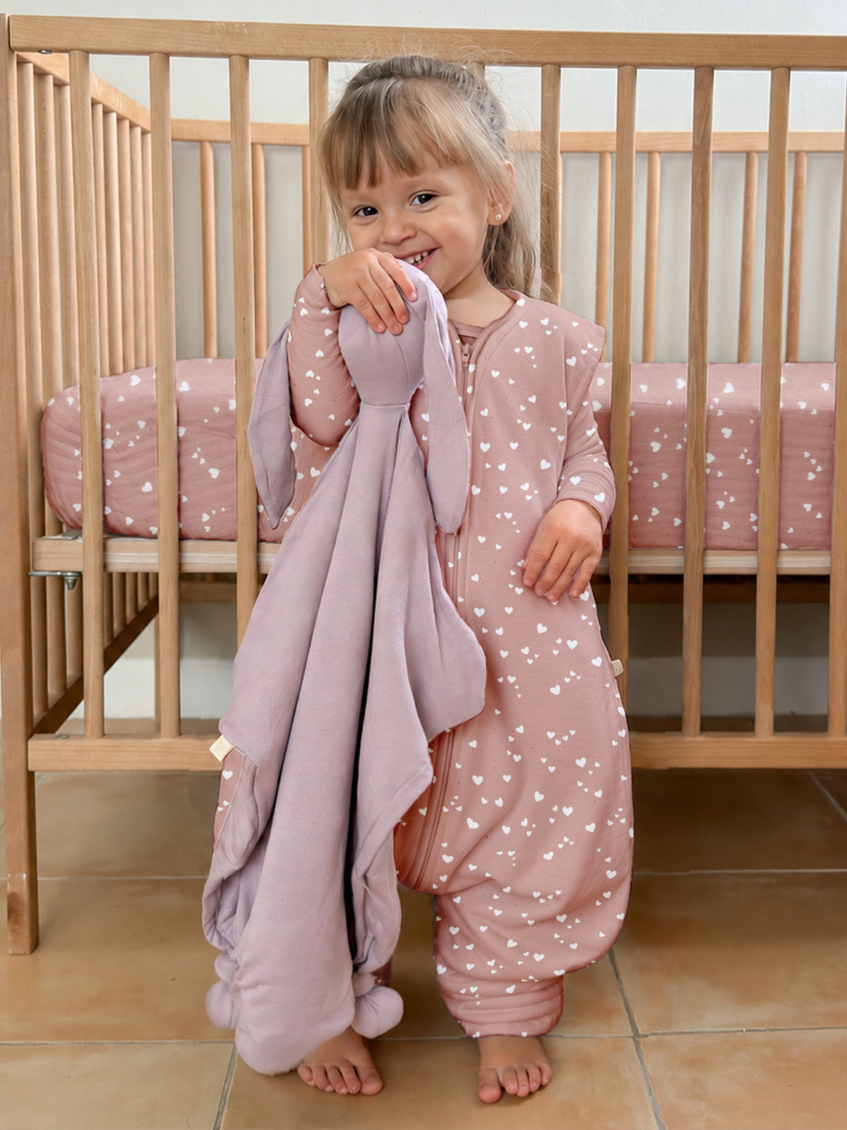 Pink heart-patterned footie sleep sack with long sleeves and enclosed feet, front view