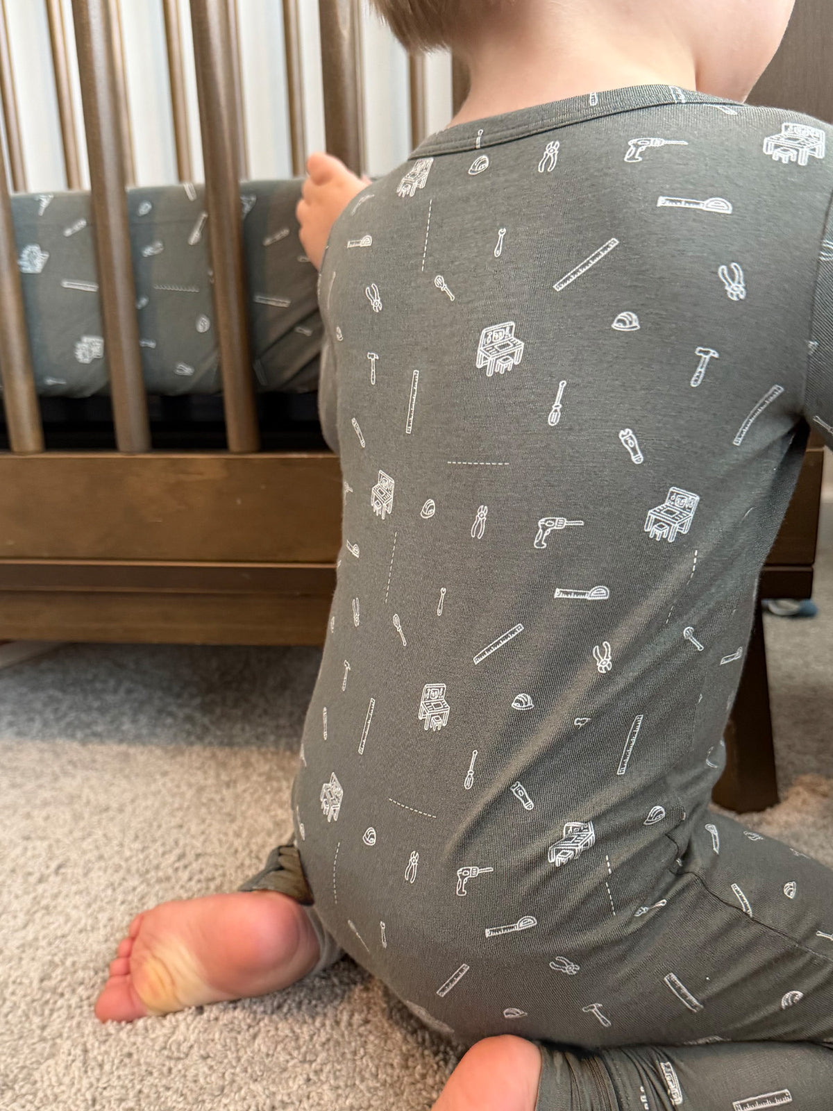 Convertible dark gray pajama with white tool icons, all-over pattern, toddler standing back view