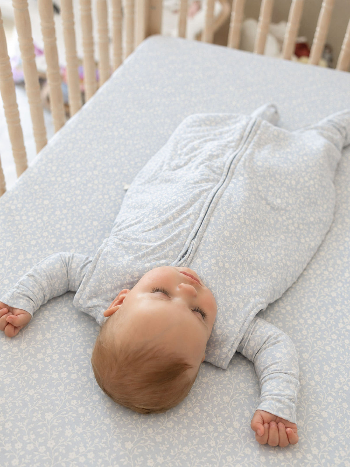 Light blue floral crib sheet with white sprig pattern, baby lying on top