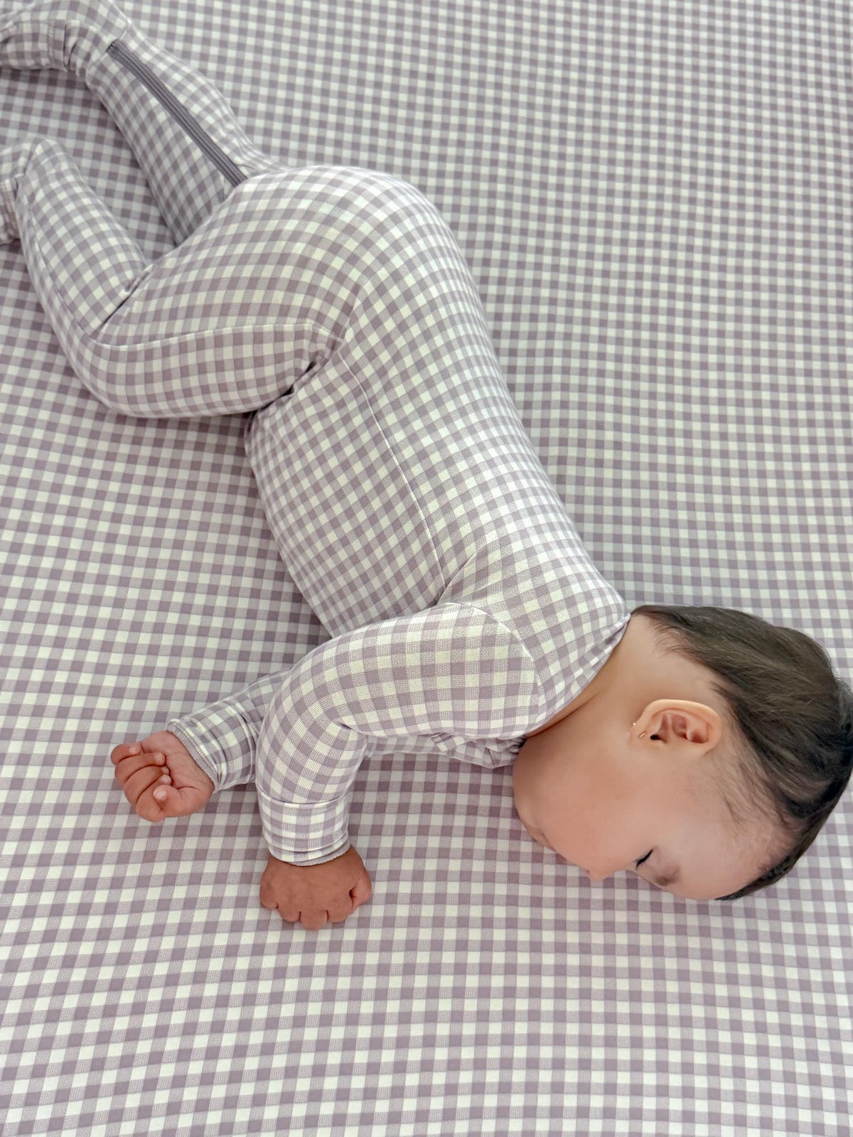 Crib sheet with light purple and white gingham pattern, baby lying on top