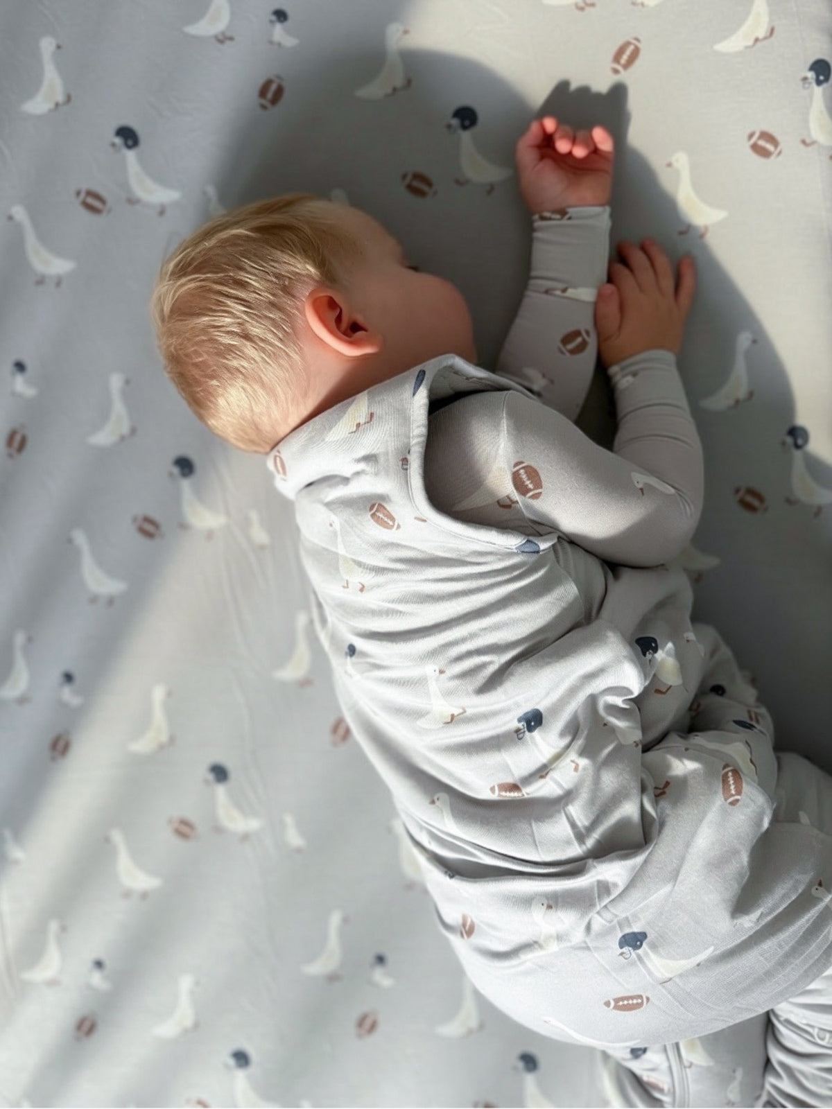 Kids footie sleep sack, light gray with football and goose prints, toddler wearing in profile