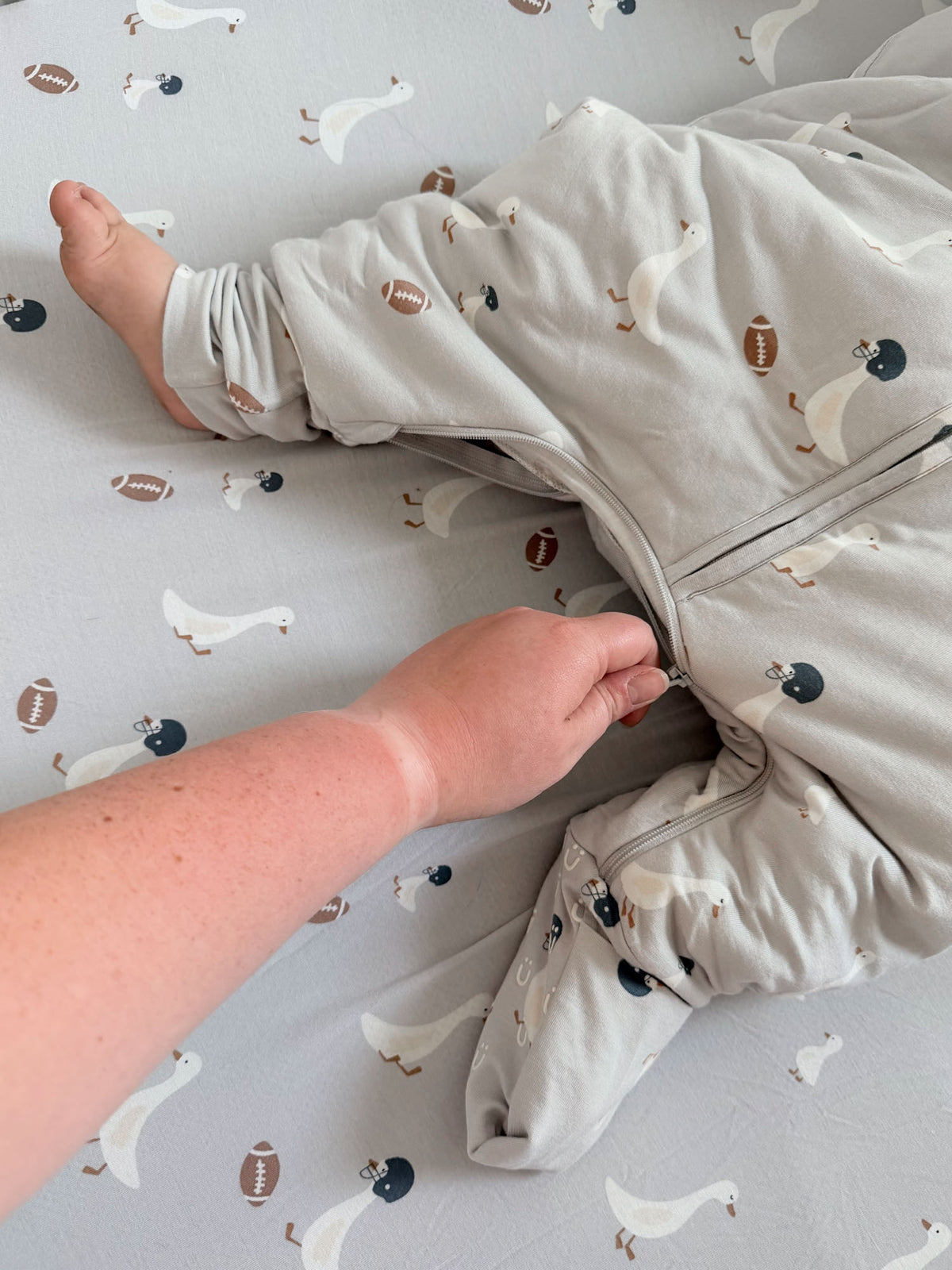 Kids long-sleeve footie sleep sack, goose and football print, close-up with zipper.