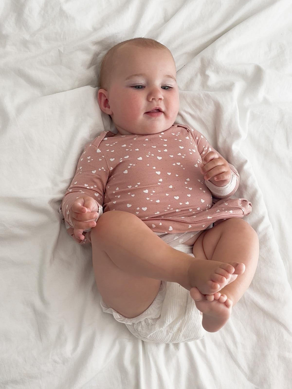 Mauve heart-print long-sleeve pajama romper on baby, snug fit