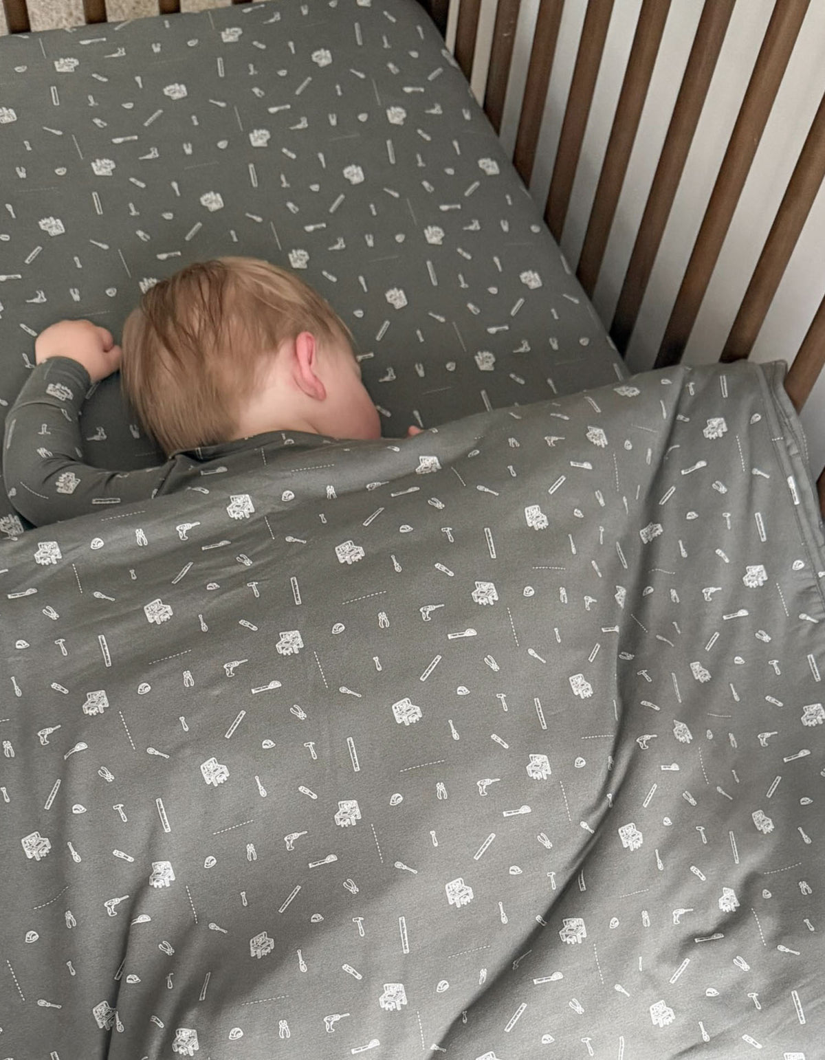 Gray baby blanket with tool pattern, baby lying under the folded blanket
