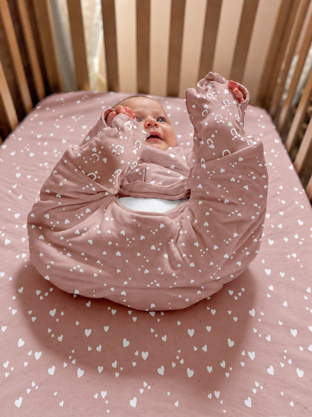 Pink heart-patterned footie sleep sack, folded, with long sleeves and enclosed feet