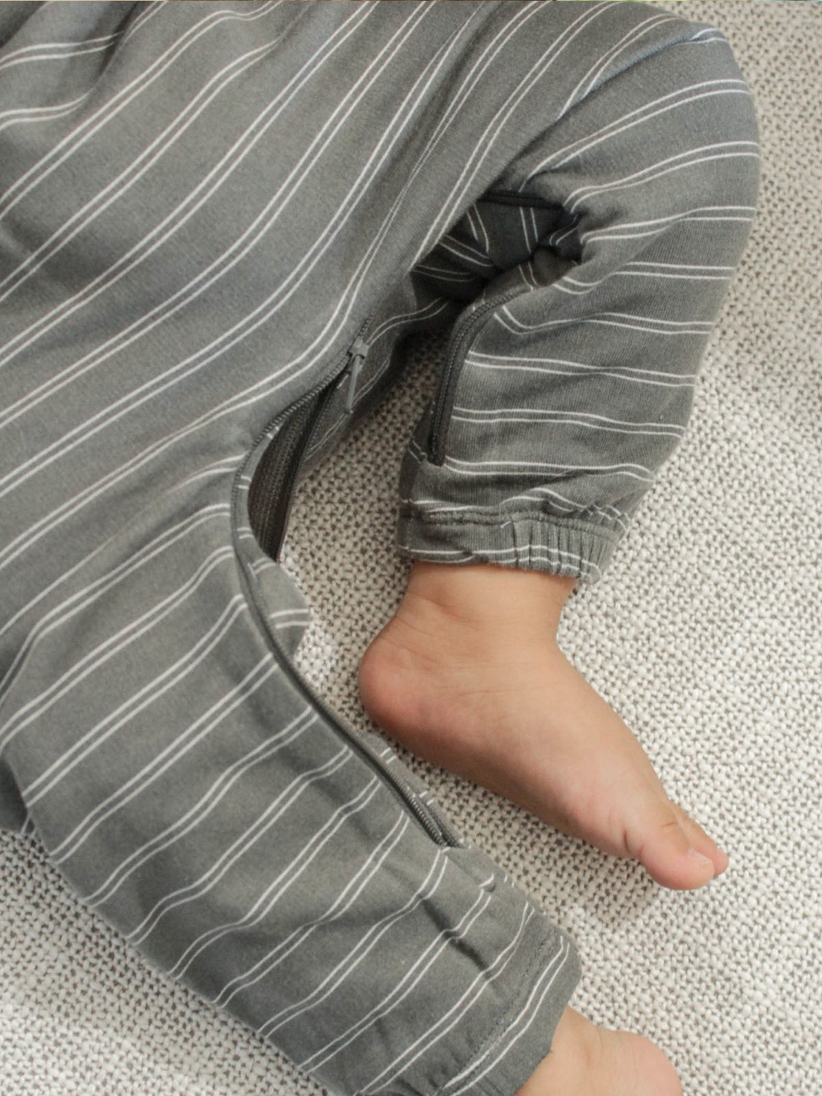 Gray striped jumpsuit sleeve cuff and hand resting on fabric, close-up