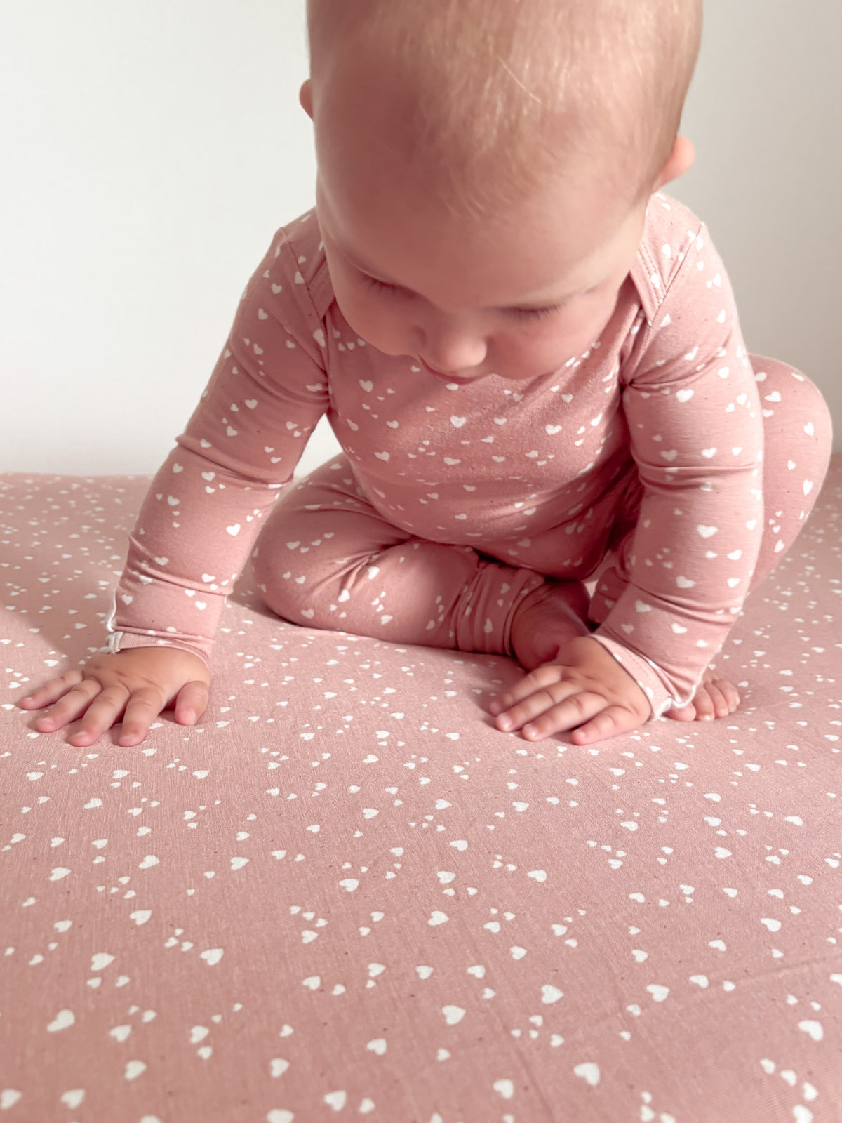Dusty rose crib sheet with tiny heart print, baby on hands and knees