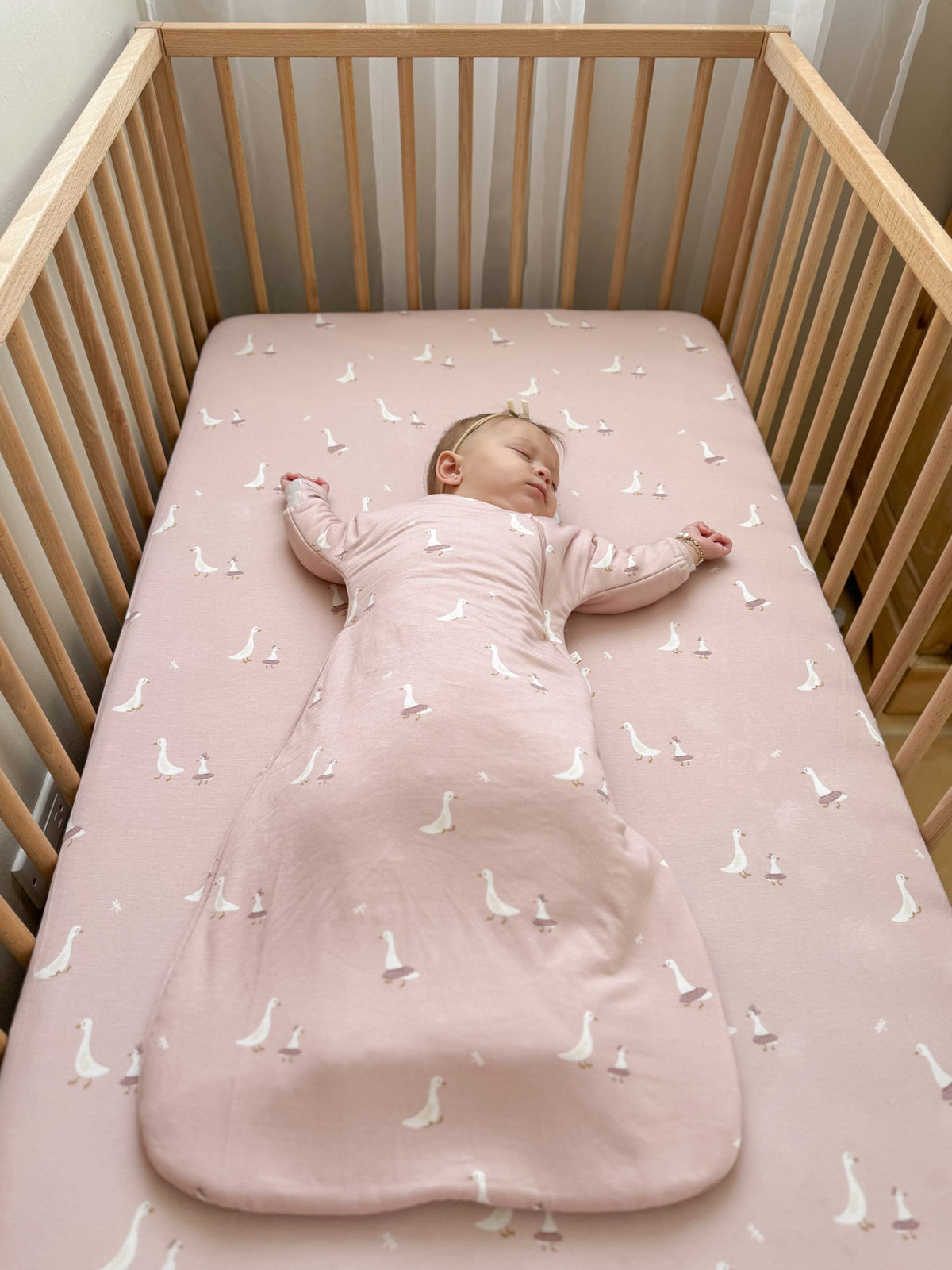 Dusty pink swaddle sack with white goose print, laid flat in crib