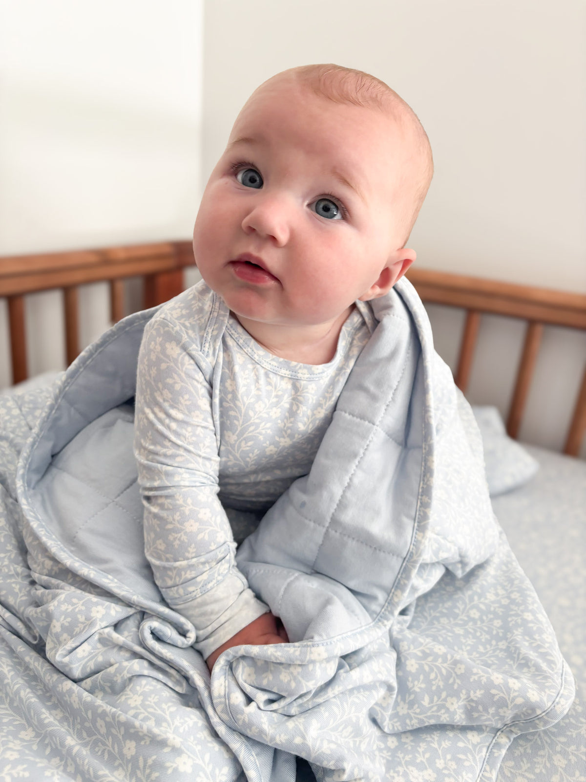 Light blue floral baby blanket with hood and front opening, baby looking up