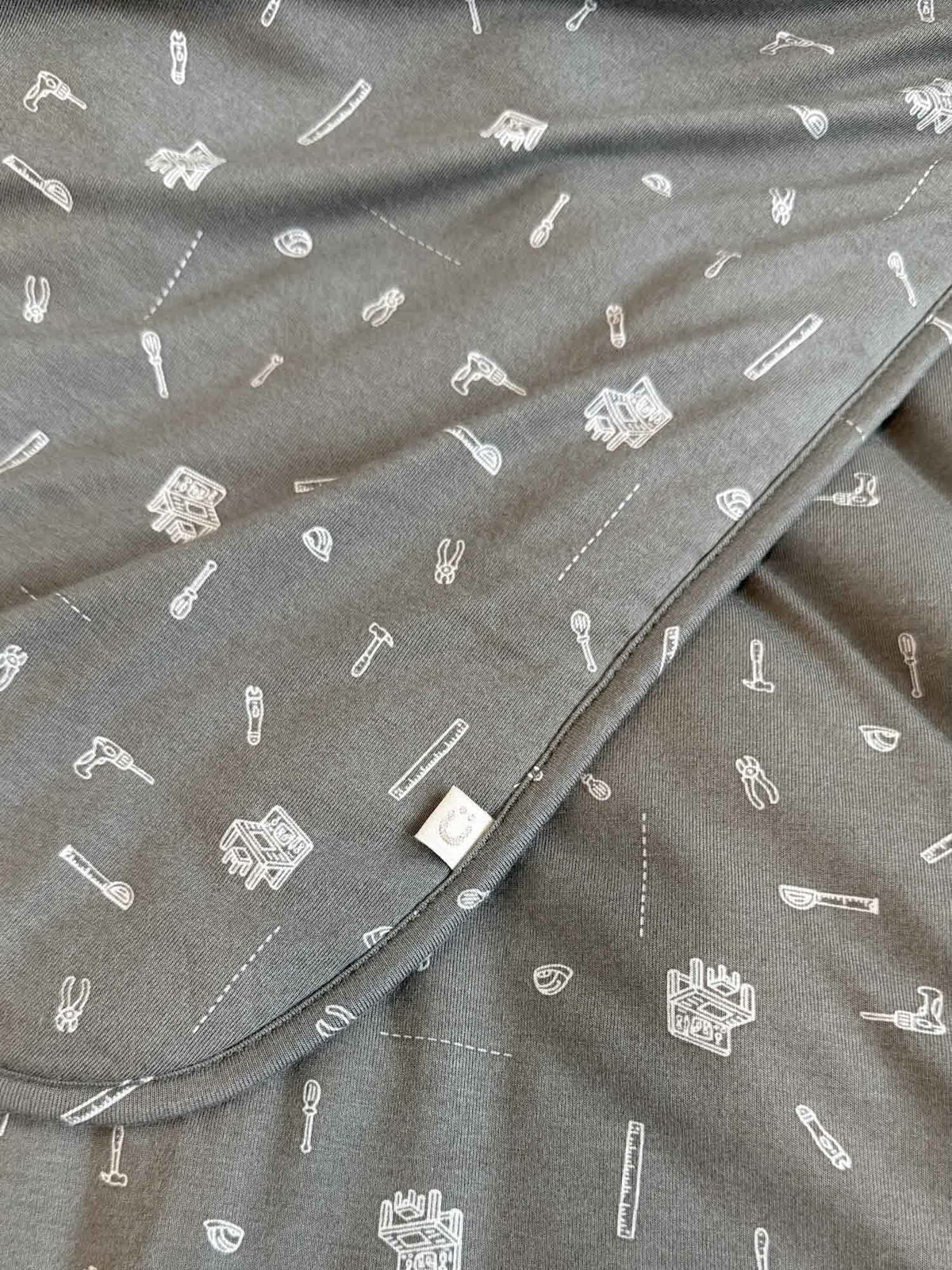 Gray blanket fabric with small tool icons and stitched corner label