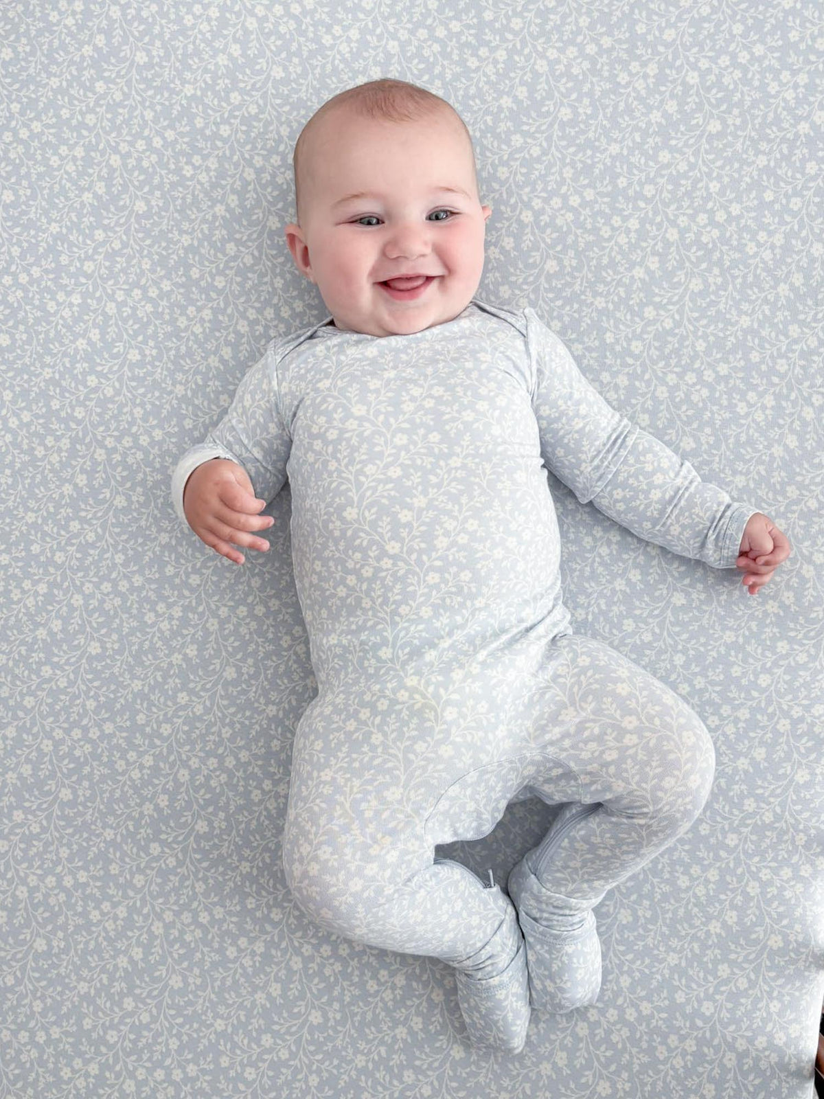 Light blue floral footed convertible pajamas with long sleeves on standing baby.